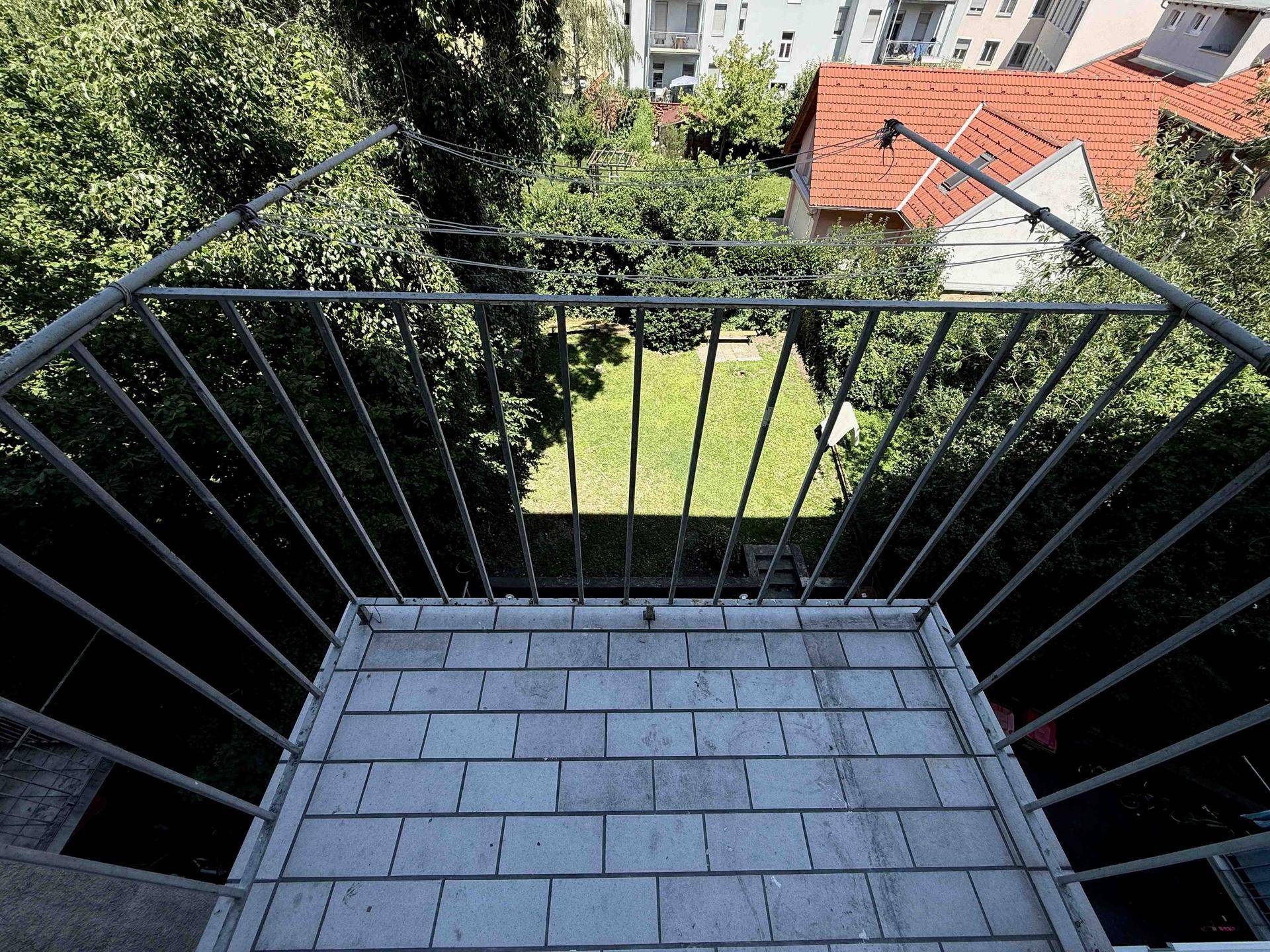 Blick von einem Balkon mit Fliesenboden auf einen gepflegten Gemeinschaftsgarten mit Rasenfläche.