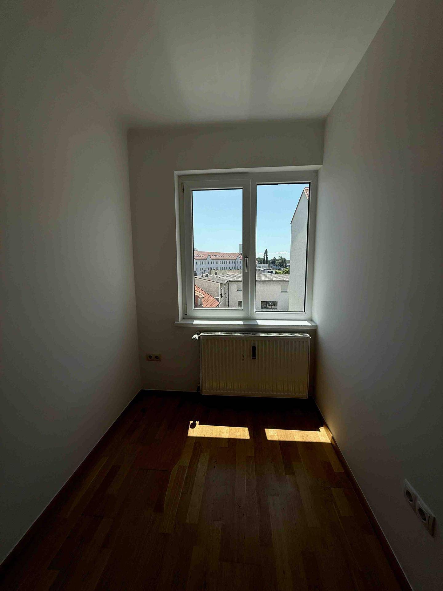 Heller Raum mit Parkettboden und Fenster, das einen weiten Blick über die Stadt ermöglicht.