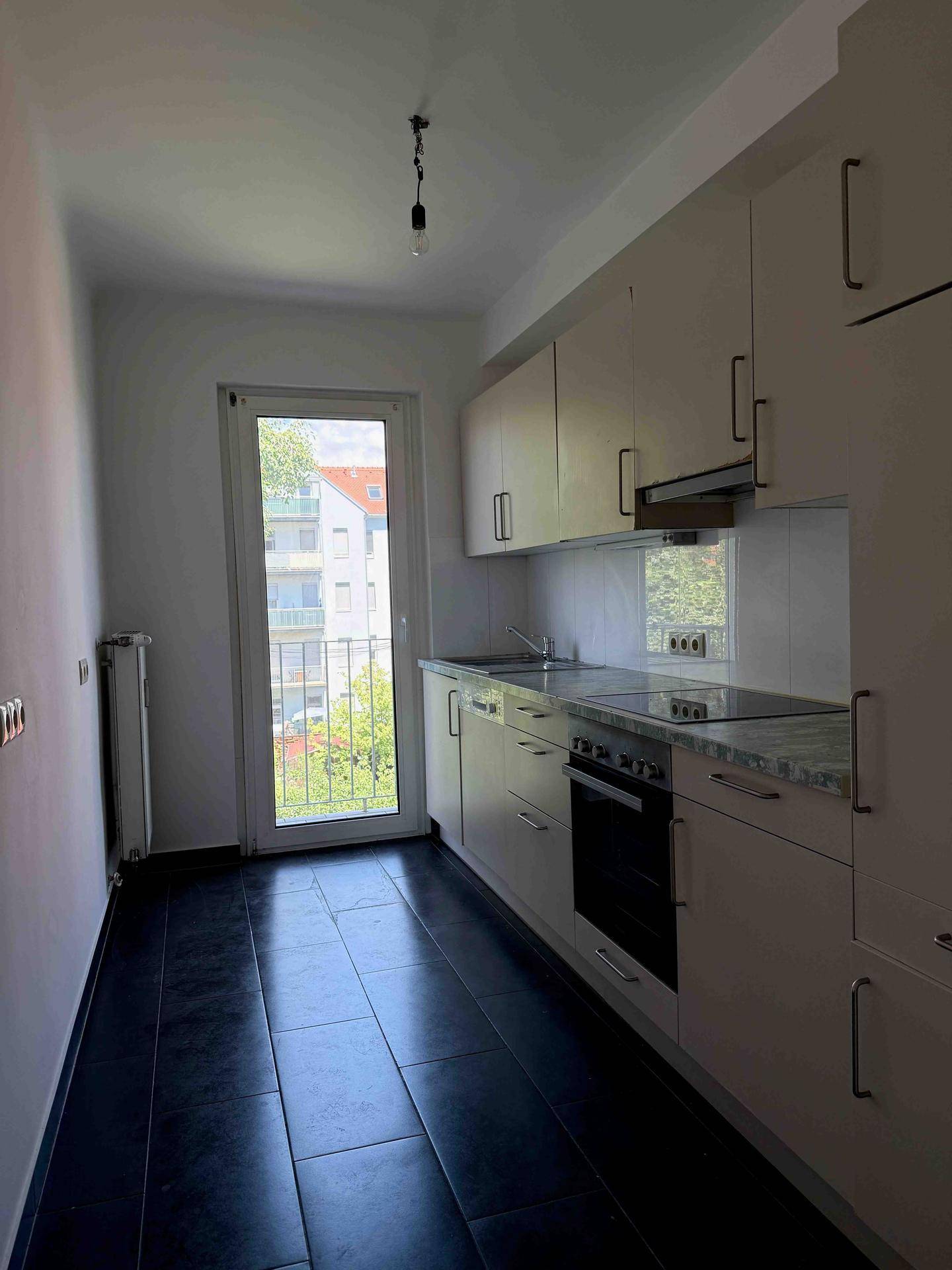 Helle Einbauküche mit beigen Schränken, dunklem Fliesenboden und Zugang zu einem kleinen Balkon.