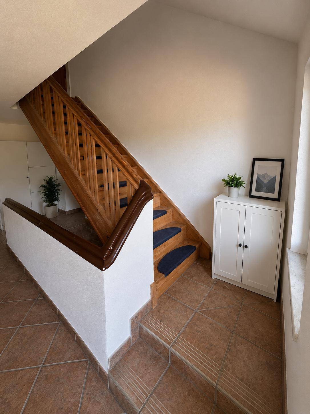 Holztreppe mit blauen Teppichläufern und Fliesenboden im Eingangsbereich.