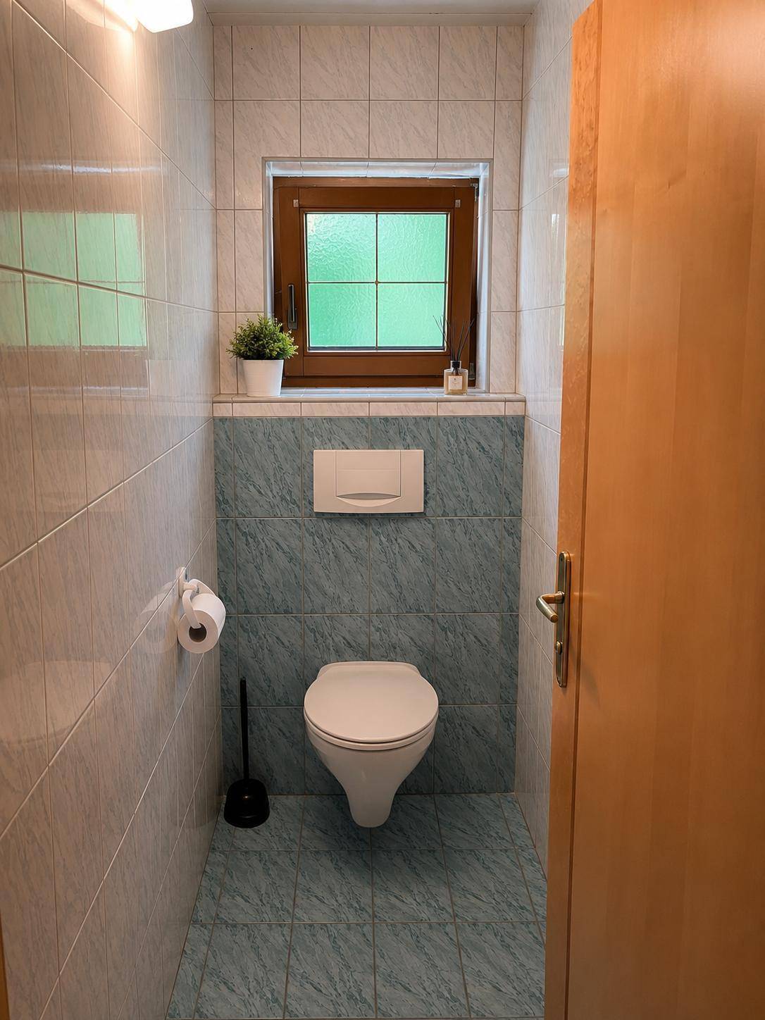 Kleines Gäste-WC mit Fliesenboden, Wand-WC und Fenster für Tageslicht.