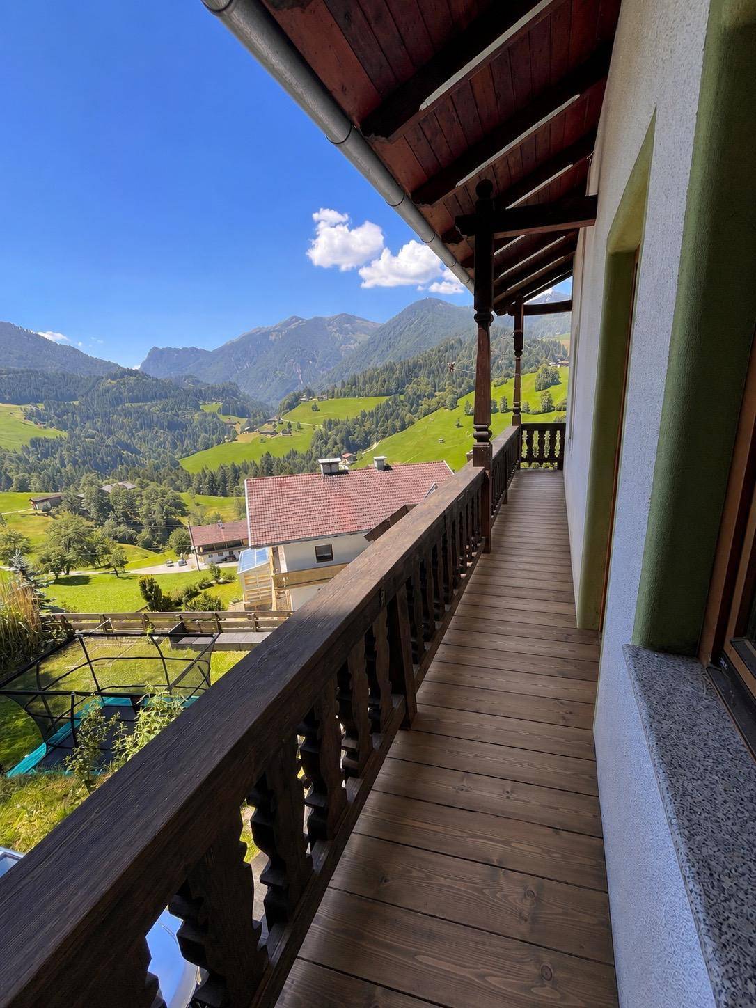 Langer Holzbalkon mit traditionellem Geländer und atemberaubendem Bergblick.
