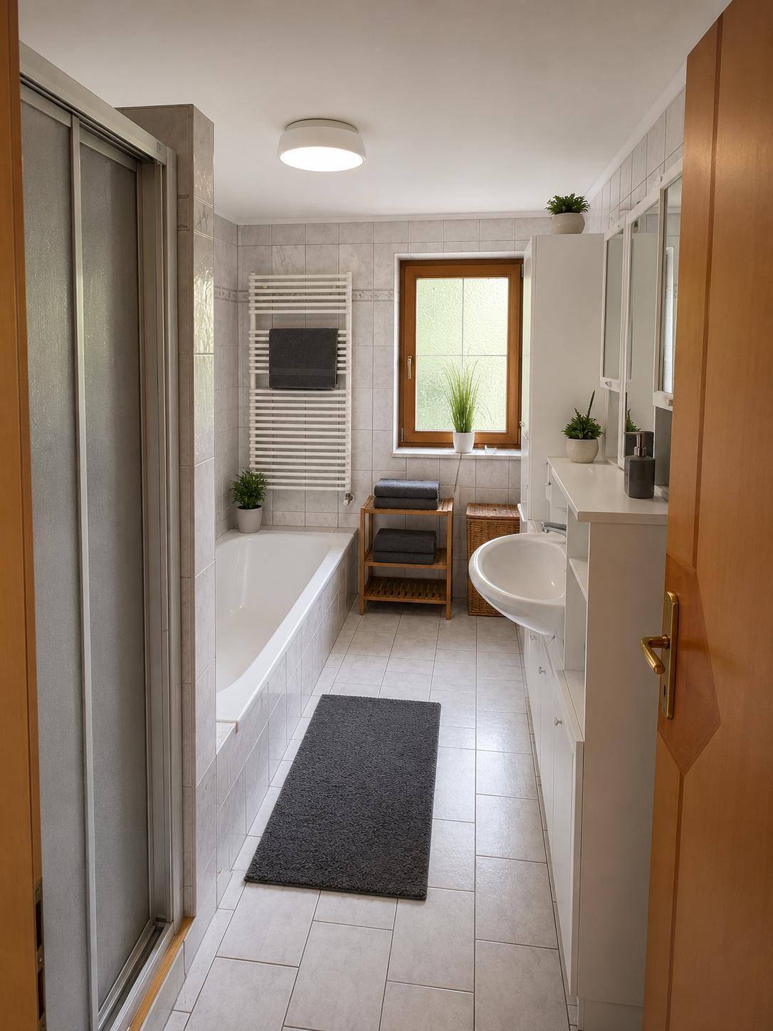 Helles Badezimmer mit Badewanne, Dusche, Waschbecken und beheiztem Handtuchhalter.