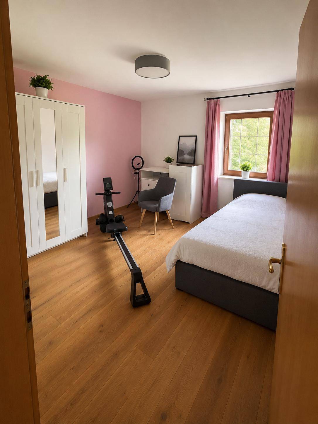 Helles Schlafzimmer mit Einzelbett, Kleiderschrank und Sportgerät, mit rosa Akzentwand.