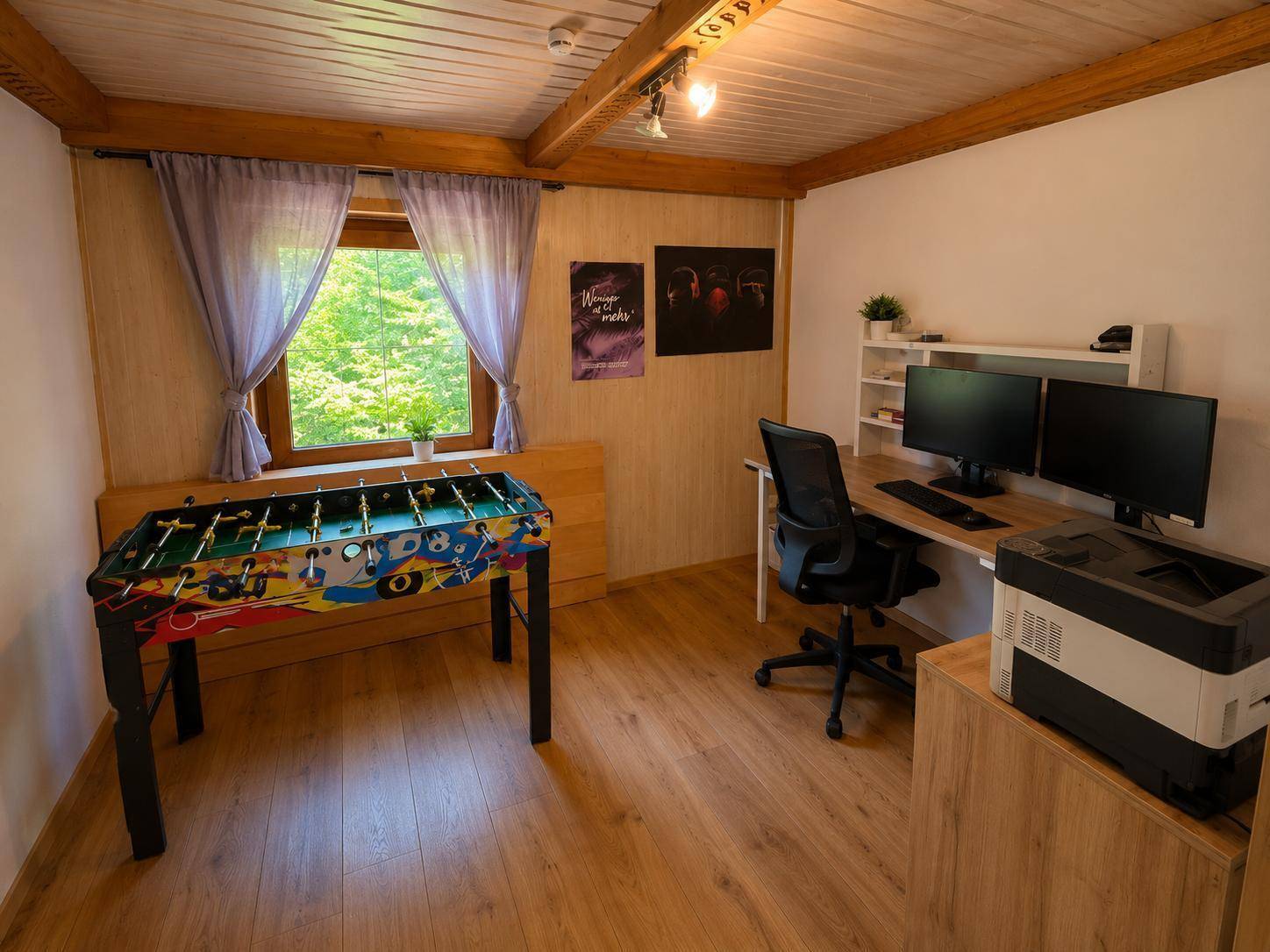 Vielseitiger Raum mit Schreibtisch, Computern und Tischfußball, ideal als Büro oder Hobbyraum.