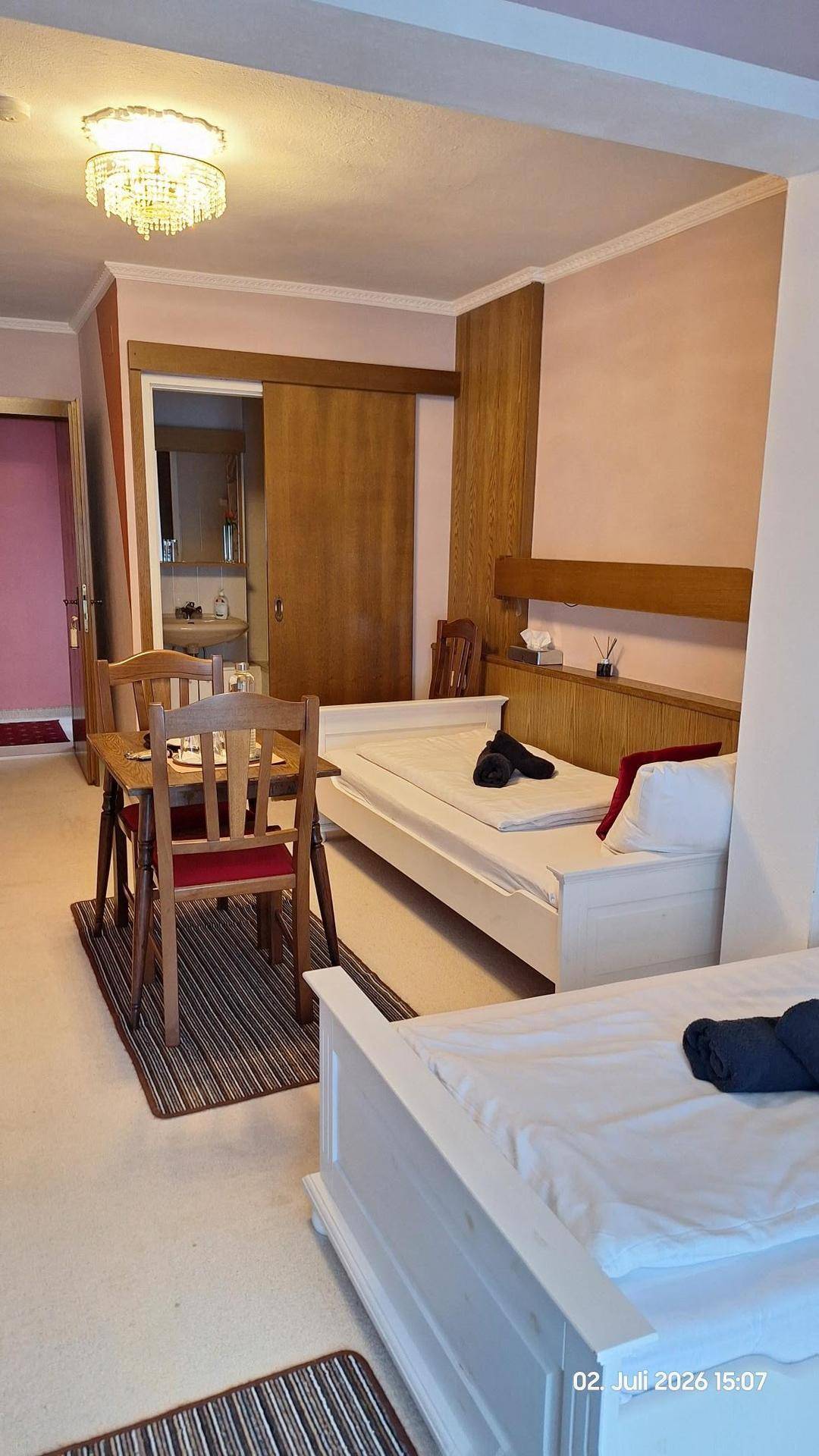 Helles Schlafzimmer mit zwei Einzelbetten, einem kleinen Esstisch und Zugang zum Badezimmer.