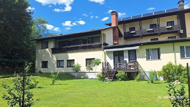 Weitläufiger grüner Gartenbereich hinter dem Gebäude mit Bäumen und einer kleinen Terrasse mit Holztreppe.