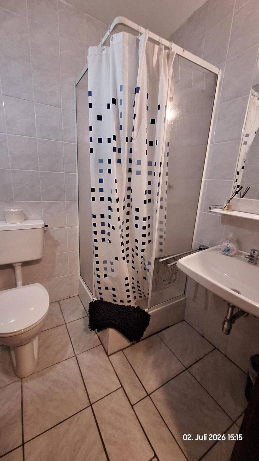 Badezimmer mit Duschkabine, Toilette und Waschbecken, ausgestattet mit hellen Fliesen.