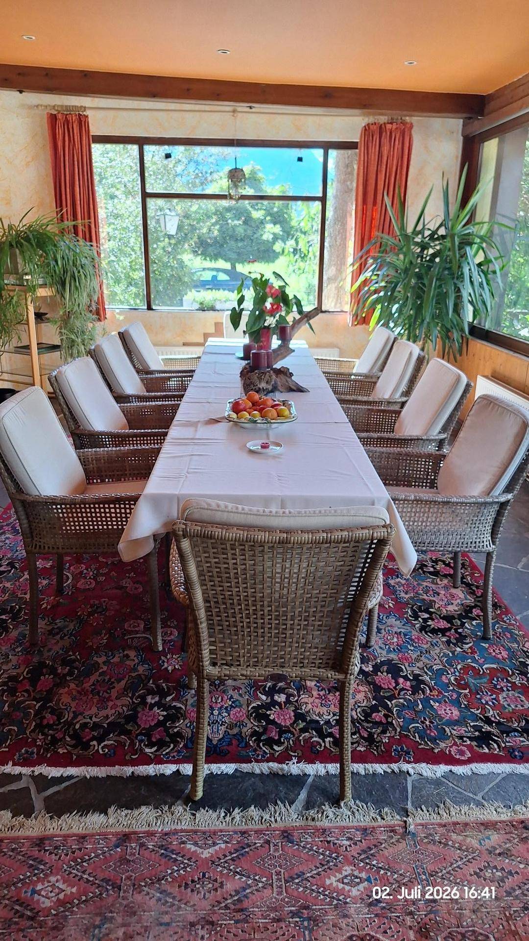 Detailansicht des gedeckten Esstisches mit Korbstühlen und einem schönen Ausblick durch das Fenster.