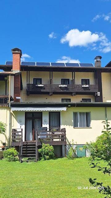 Rückseite des Gebäudes mit Balkonen, einer Holztreppe und Solarpaneelen auf dem Dach, umgeben von einem grünen Garten.