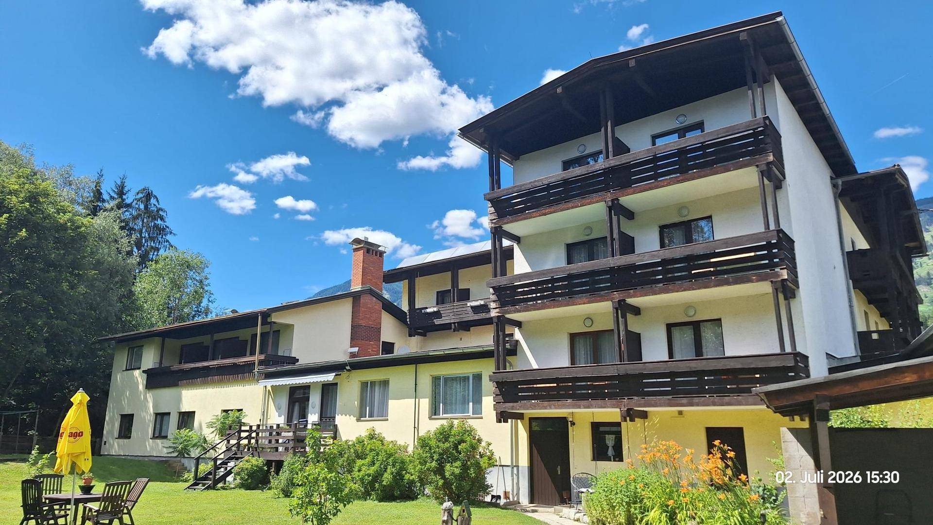 Rückseite des Hotels mit mehreren Balkonen und einem gepflegten Gartenbereich mit Sitzgelegenheiten.