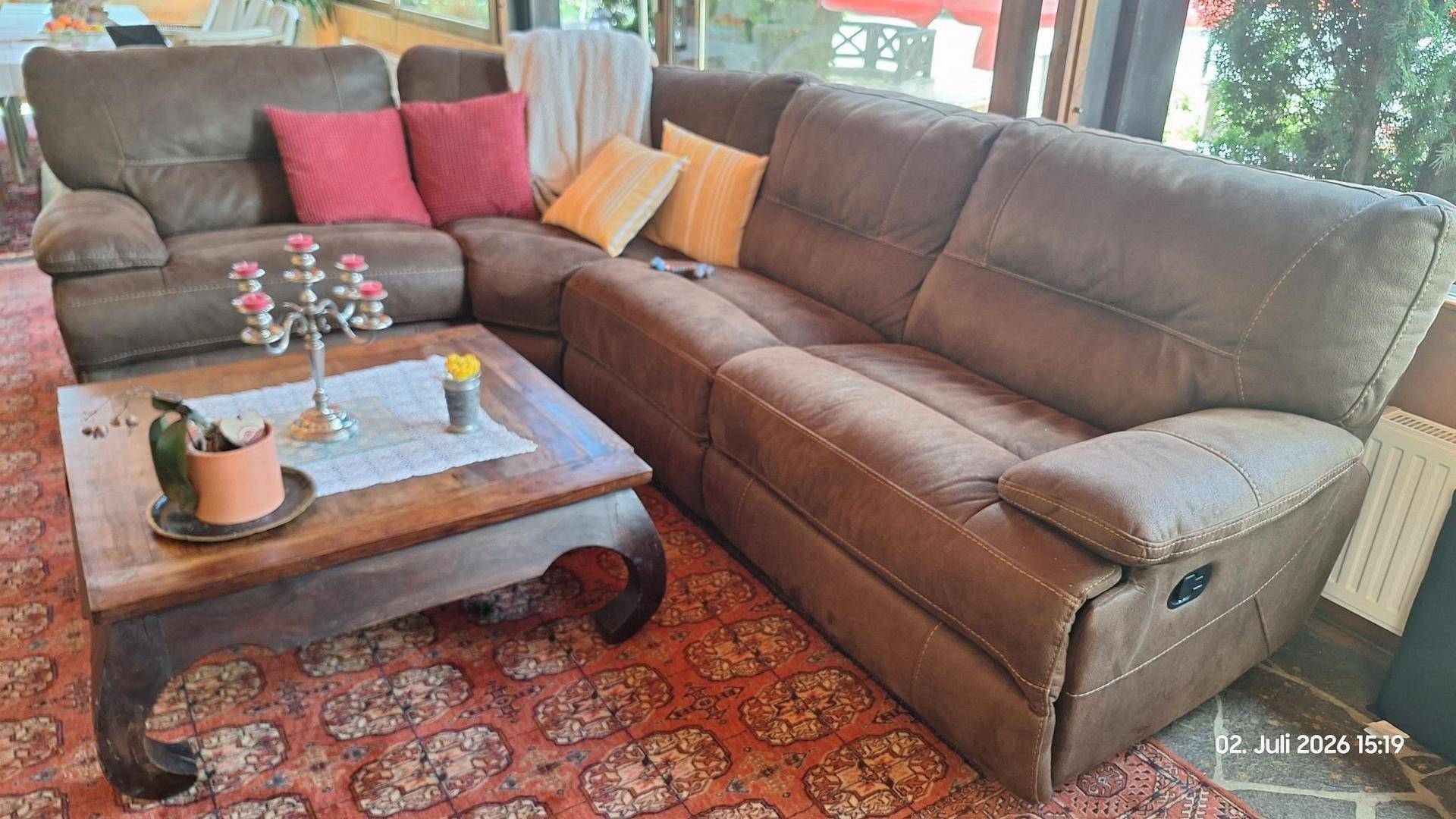 Gemütliches Wohnzimmer mit großem braunem Ecksofa und einem rustikalen Holztisch auf Teppichboden.