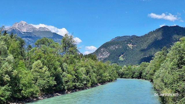 Malerische Flusslandschaft mit türkisblauem Wasser, umgeben von grünen Wäldern und majestätischen Bergen.