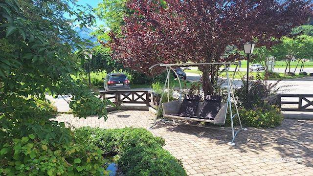 Einladender Gartenbereich mit einer Schaukelbank und reicher Vegetation neben einem gepflasterten Weg.