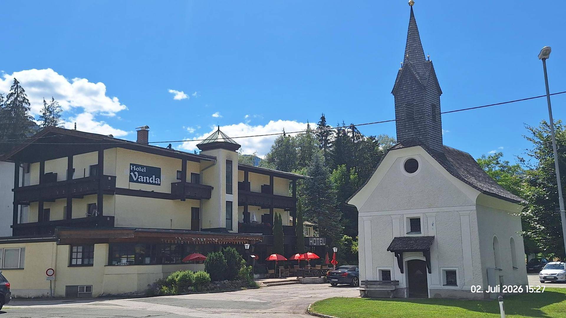 Ansicht des Hotels mit traditioneller Architektur und einer charmanten Kapelle unter blauem Himmel.