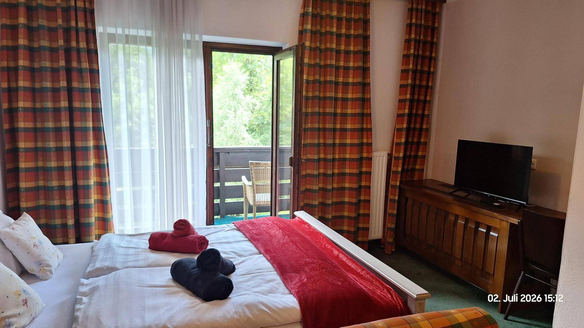 Schlafzimmer mit Doppelbett, Fernseher und direktem Zugang zu einem Balkon mit grüner Aussicht.