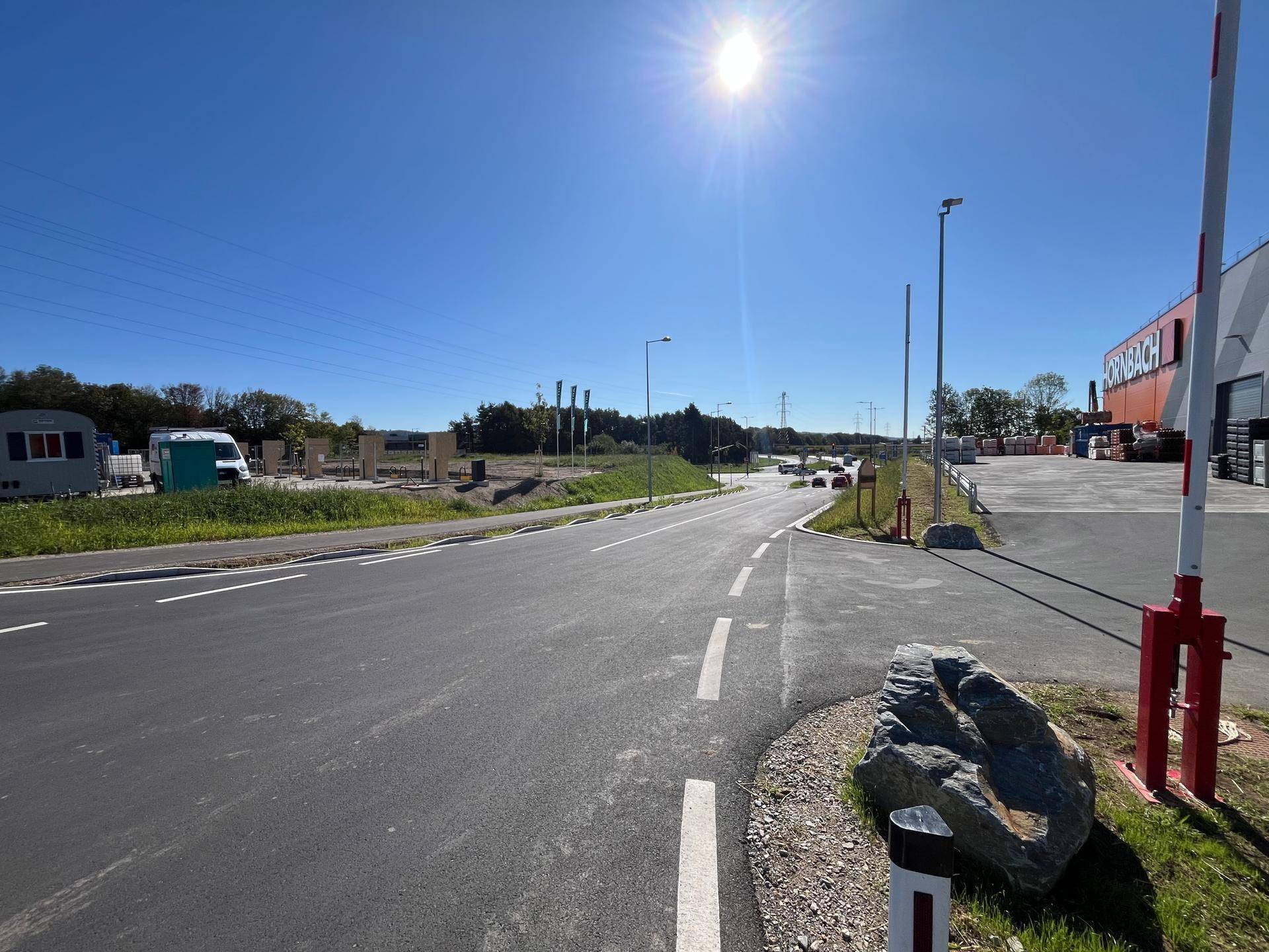 Neue Zufahrtsstraße zu einem Gewerbegebiet mit einem Baumarkt, unter strahlendem Sonnenschein und blauem Himmel.