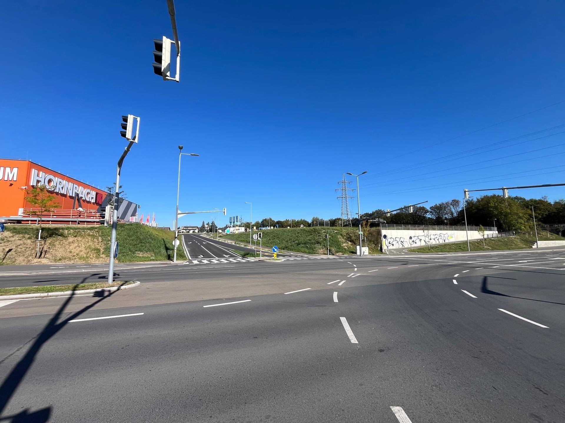 Straßenkreuzung mit Ampelanlage und einem großen Baumarkt, im Hintergrund die Infrastruktur einer Autobahn.
