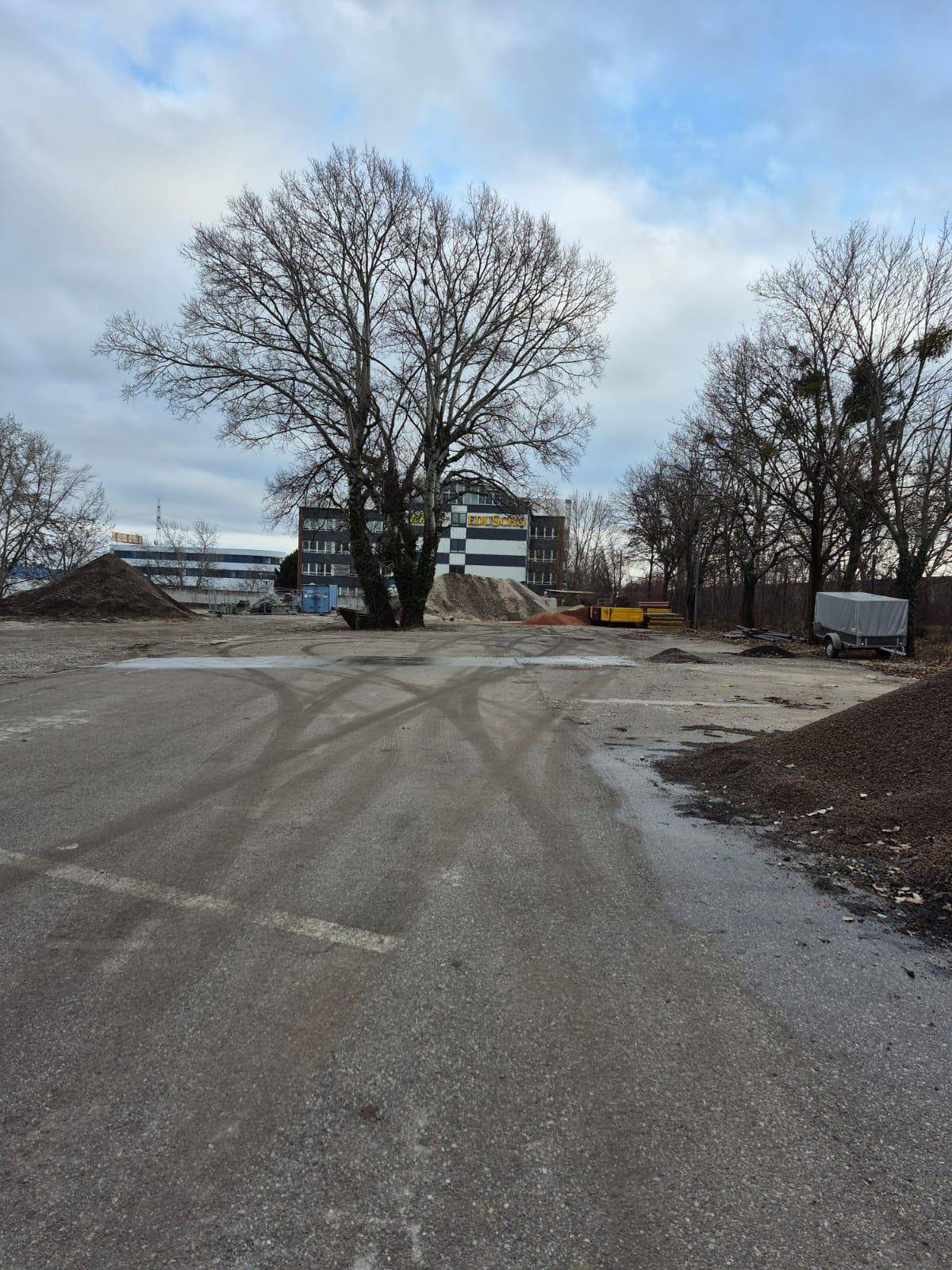 Weitläufiges Außengelände mit Schotterflächen, Erdhügeln und einem Gebäude im Hintergrund unter bewölktem Himmel.