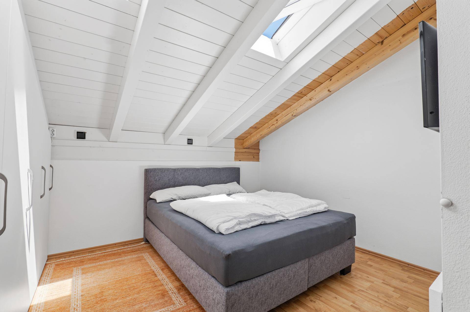 Gemütliches Schlafzimmer im Dachgeschoss mit schrägen Wänden, Holzbalken und Dachfenster.