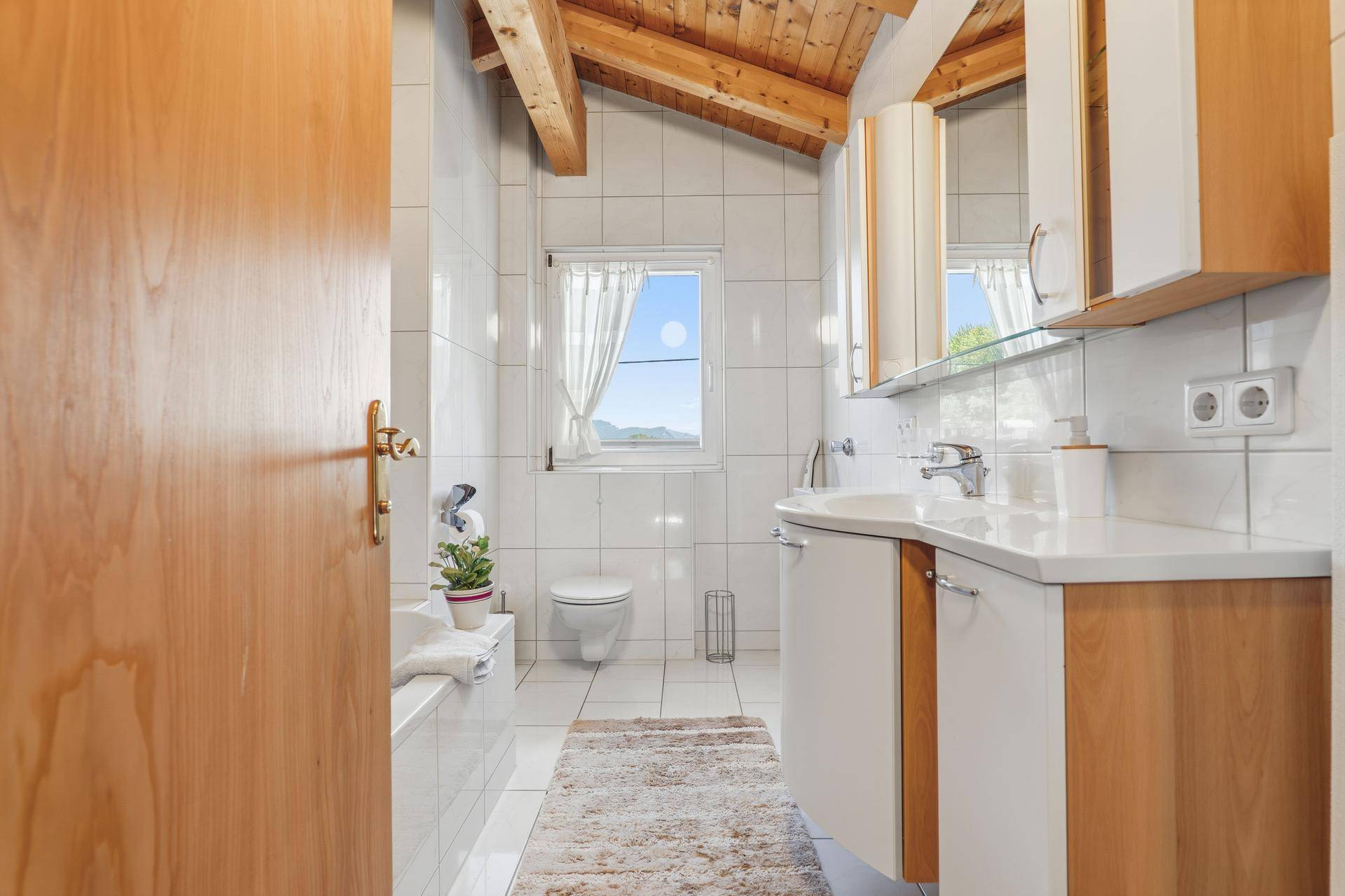 Helles Badezimmer im Dachgeschoss mit weißen Fliesen, Badewanne und Fenster.