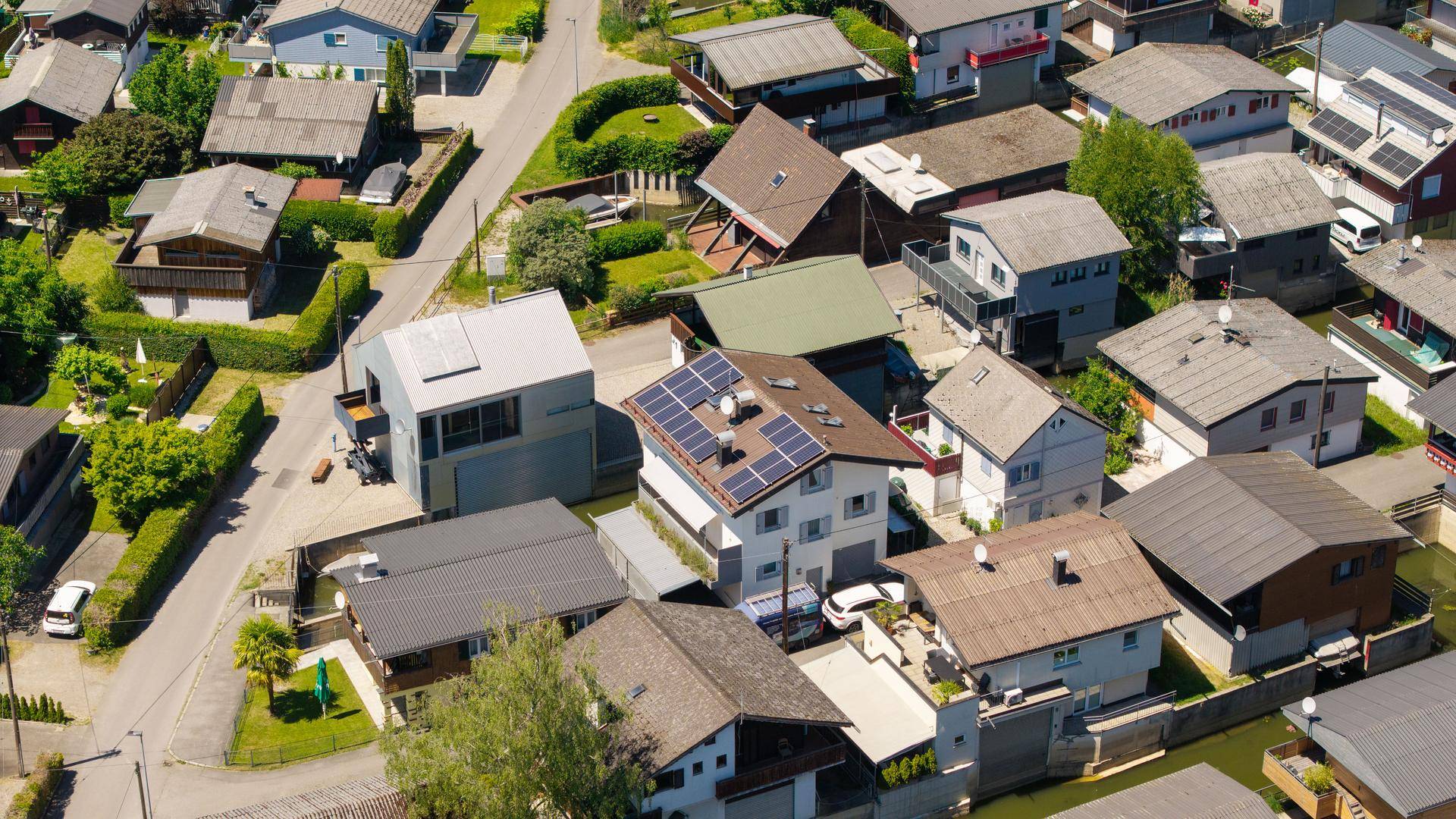Nahaufnahme von Wohnhäusern aus der Vogelperspektive, einige mit Solaranlagen auf den Dächern.