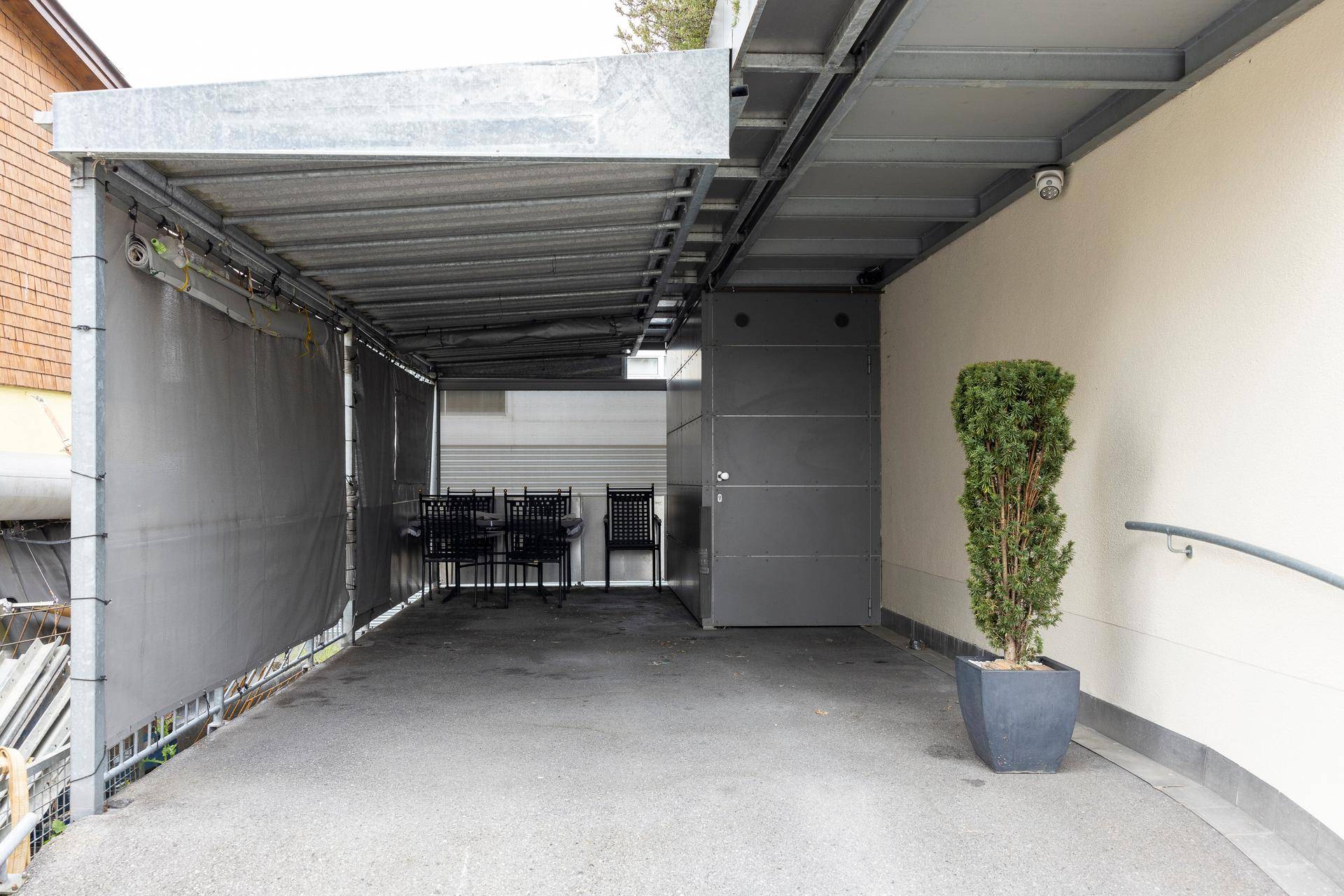 Überdachter Außenbereich, möglicherweise ein Carport oder Eingang, mit Sitzgelegenheiten.