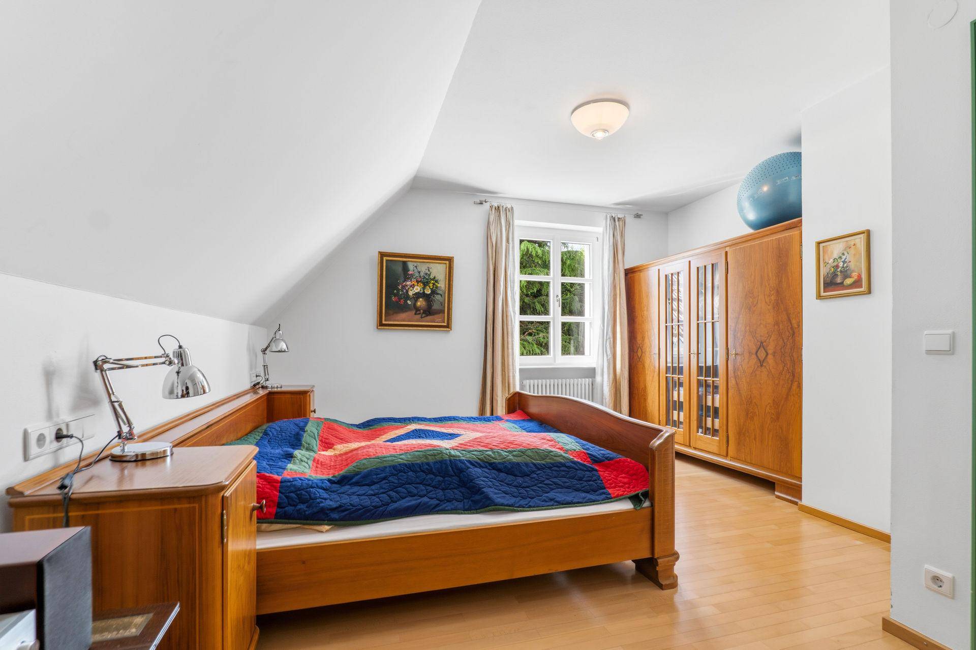 Gemütliches Schlafzimmer im Dachgeschoss mit Holzbett, Kleiderschrank und schrägen Wänden.