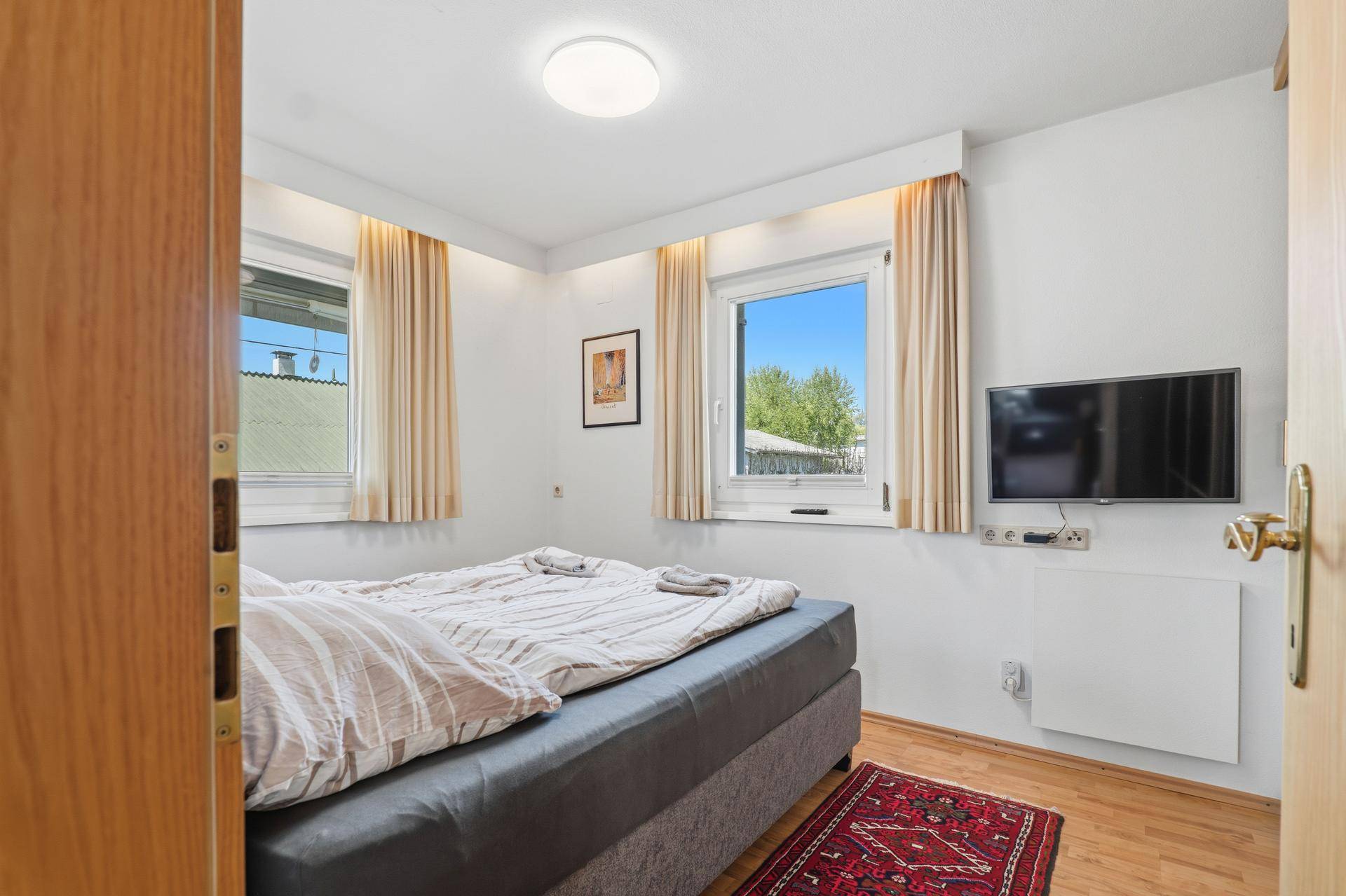Helles Schlafzimmer mit zwei Fenstern, Holzboden und einem bequemen Doppelbett.