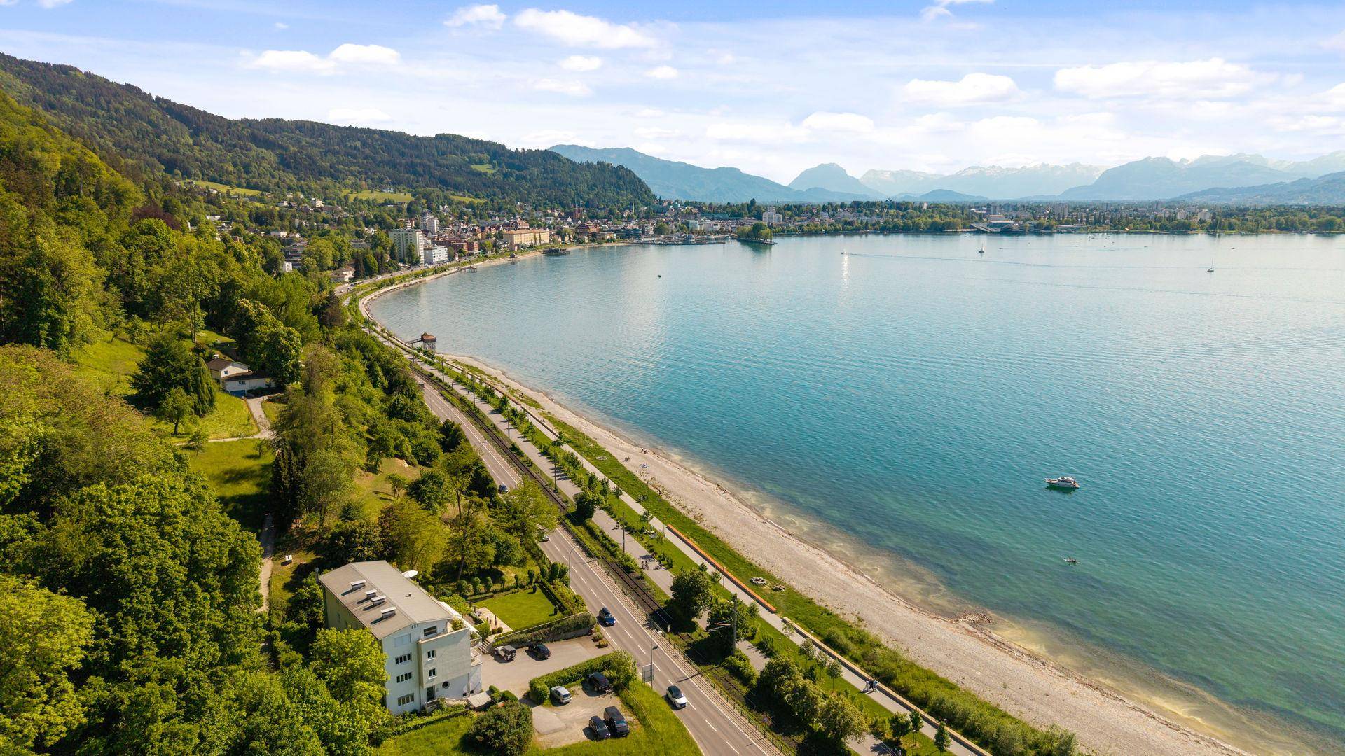 Luftaufnahme der Immobilie und Umgebung mit See, Straße und Bergen im Hintergrund.