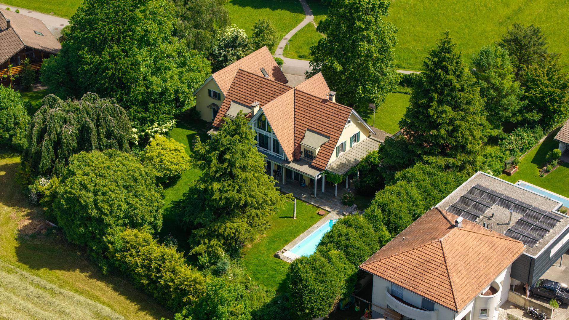 Luftaufnahme eines charmanten Hauses mit rotem Dach, umgeben von üppigem Grün und ländlicher Landschaft.