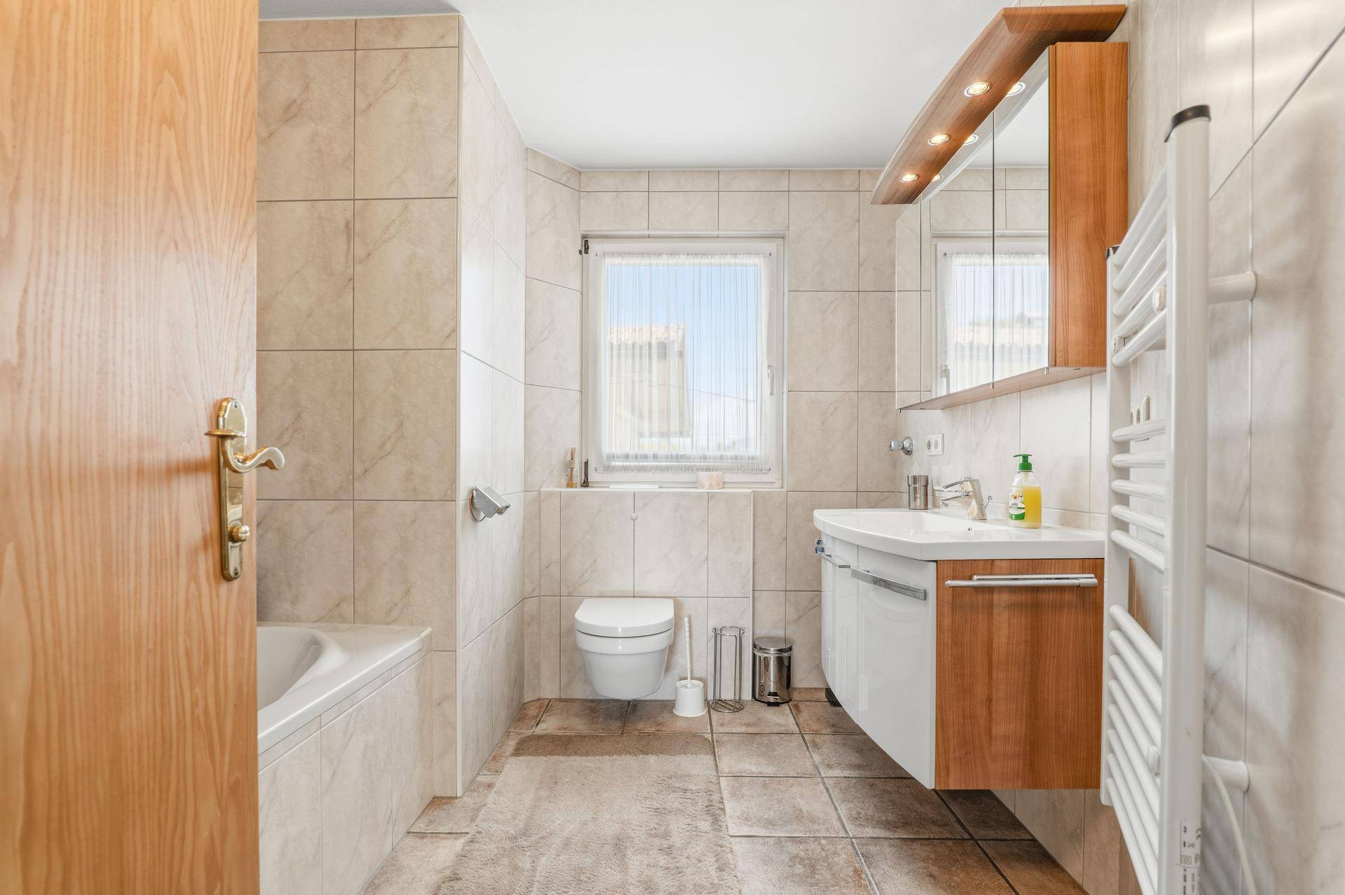 Gefliestes Badezimmer mit Badewanne, Waschbecken, WC und einem Fenster für Tageslicht.