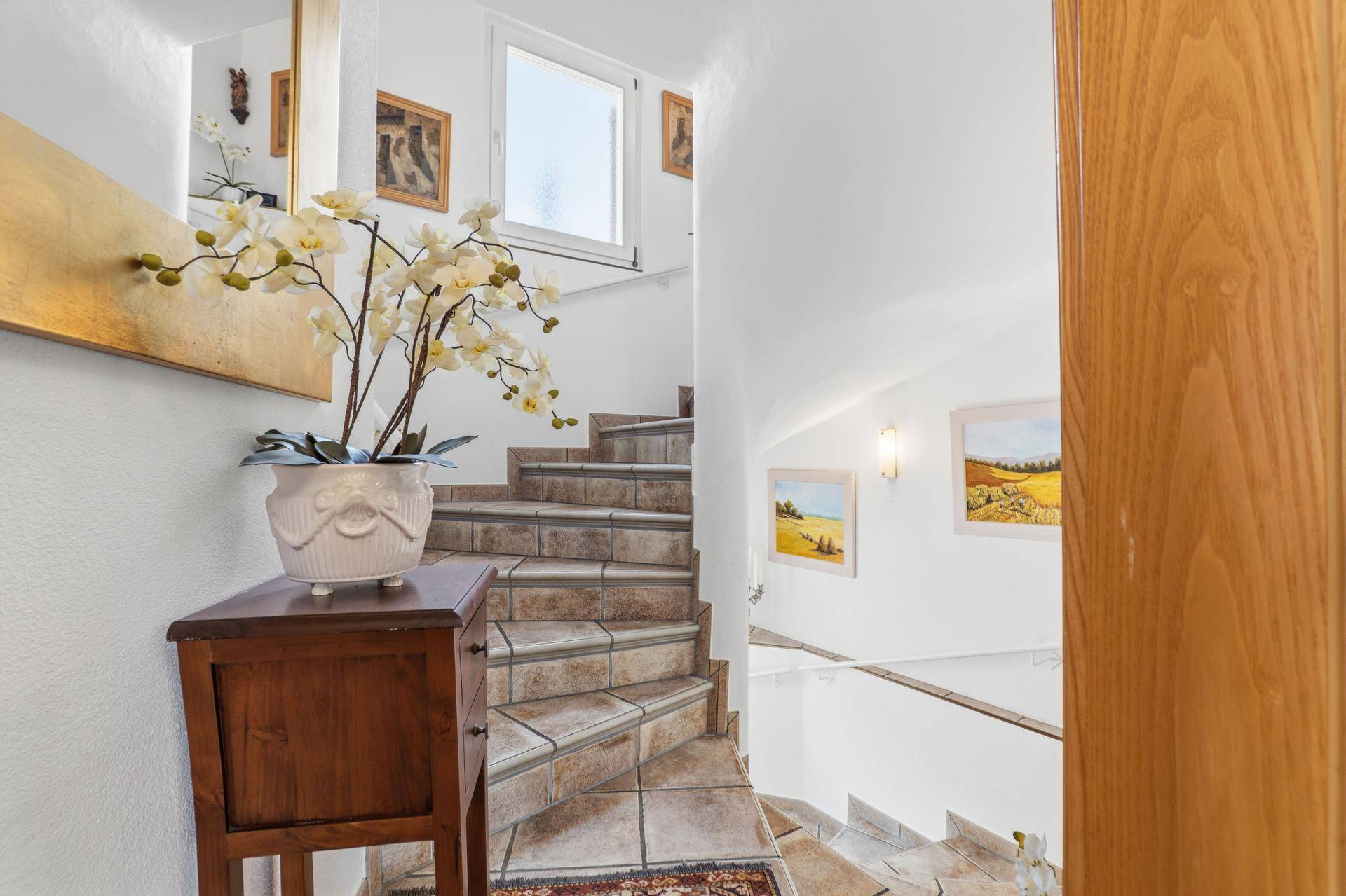 Wendeltreppe mit gefliesten Stufen und Holzgeländer, die die verschiedenen Ebenen verbindet.