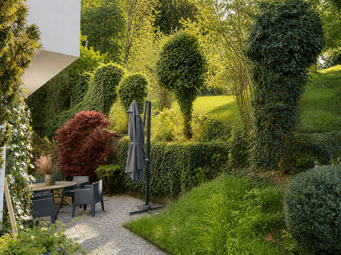 Gartenbereich mit vielfältiger Bepflanzung, Bäumen und einem kleinen Kies-Sitzbereich.