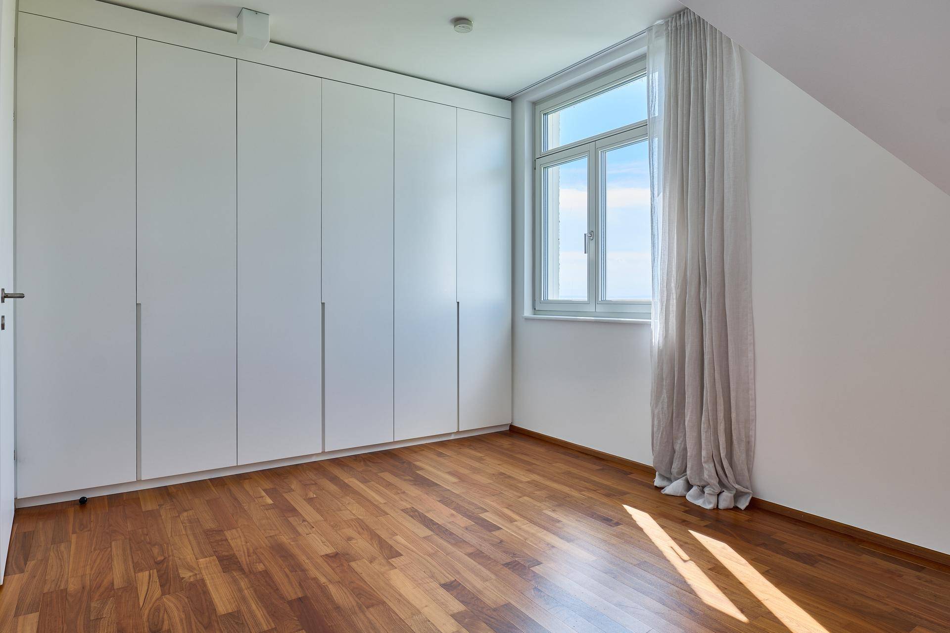 Schlafzimmer im Dachgeschoss mit einer Wand voller weißer Einbauschränke und Holzboden.