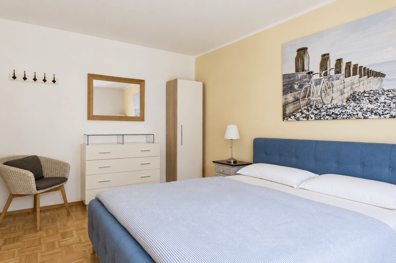 Komfortables Schlafzimmer mit blauem Polsterbett, Parkettboden und ausreichend Stauraum.