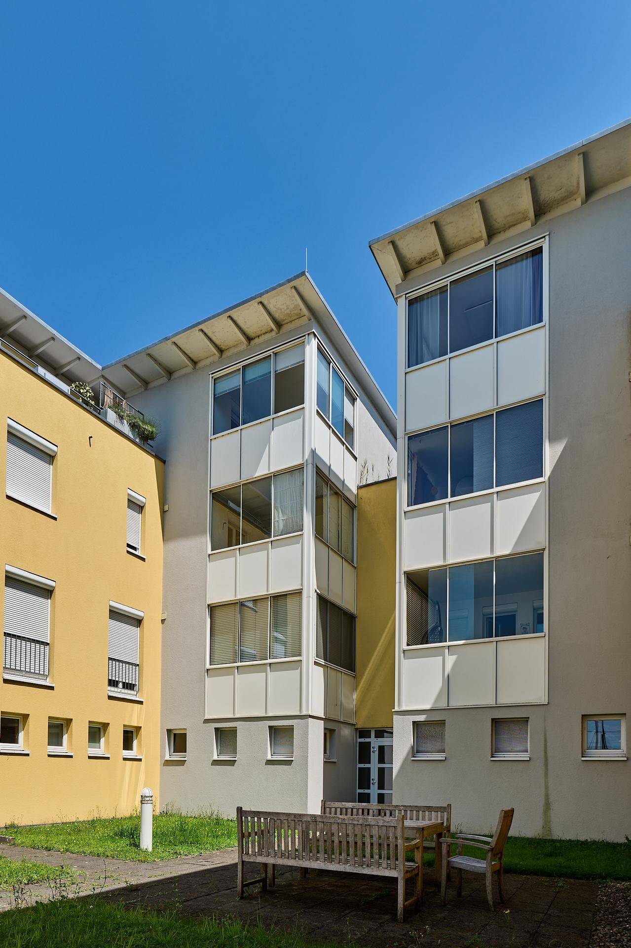 Außenansicht der modernen Apartmentgebäude von einem begrünten Innenhof mit Sitzgelegenheiten.