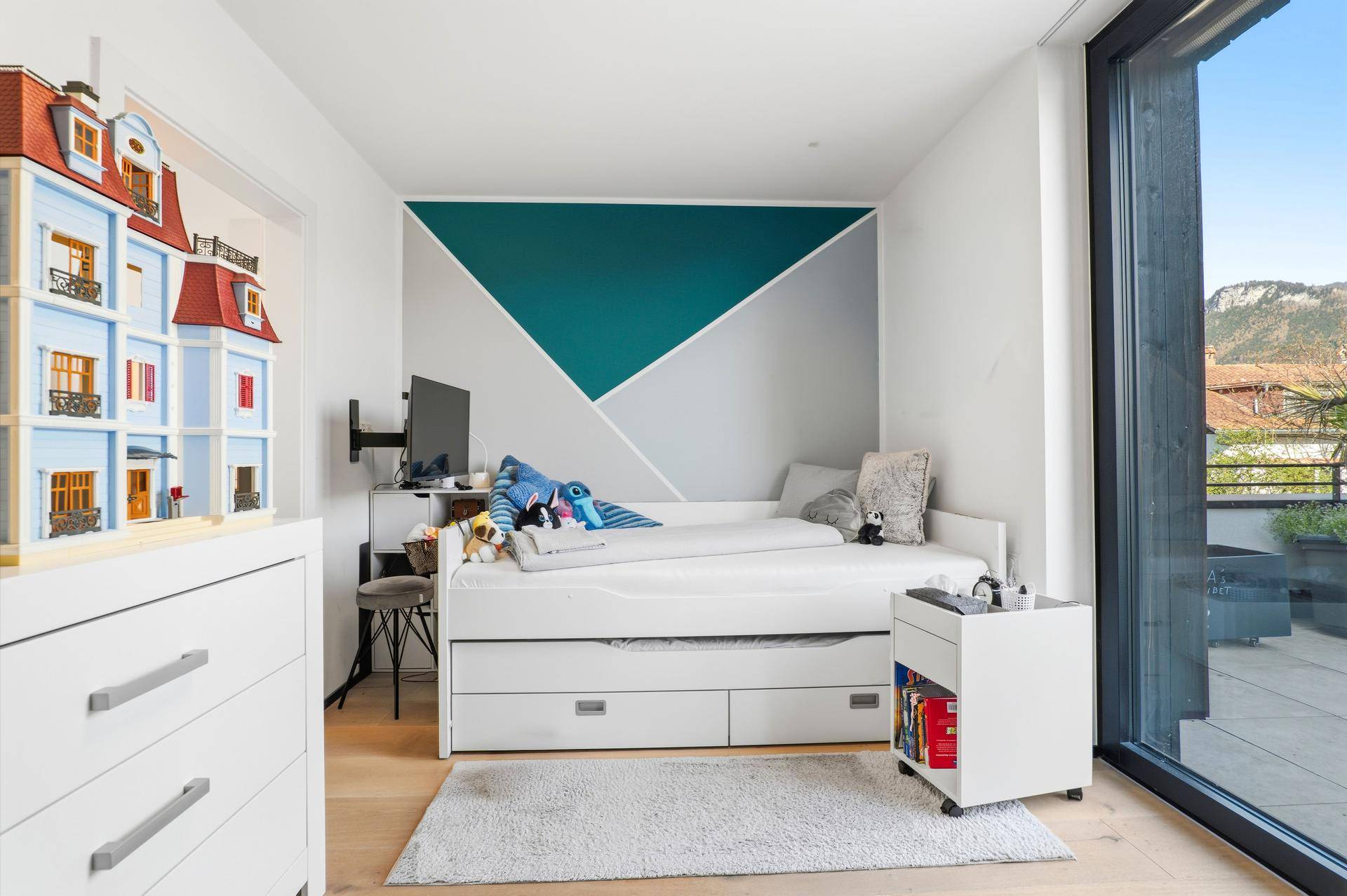 Kinderzimmer mit Einzelbett, farbiger Wandgestaltung und Zugang zur Terrasse.