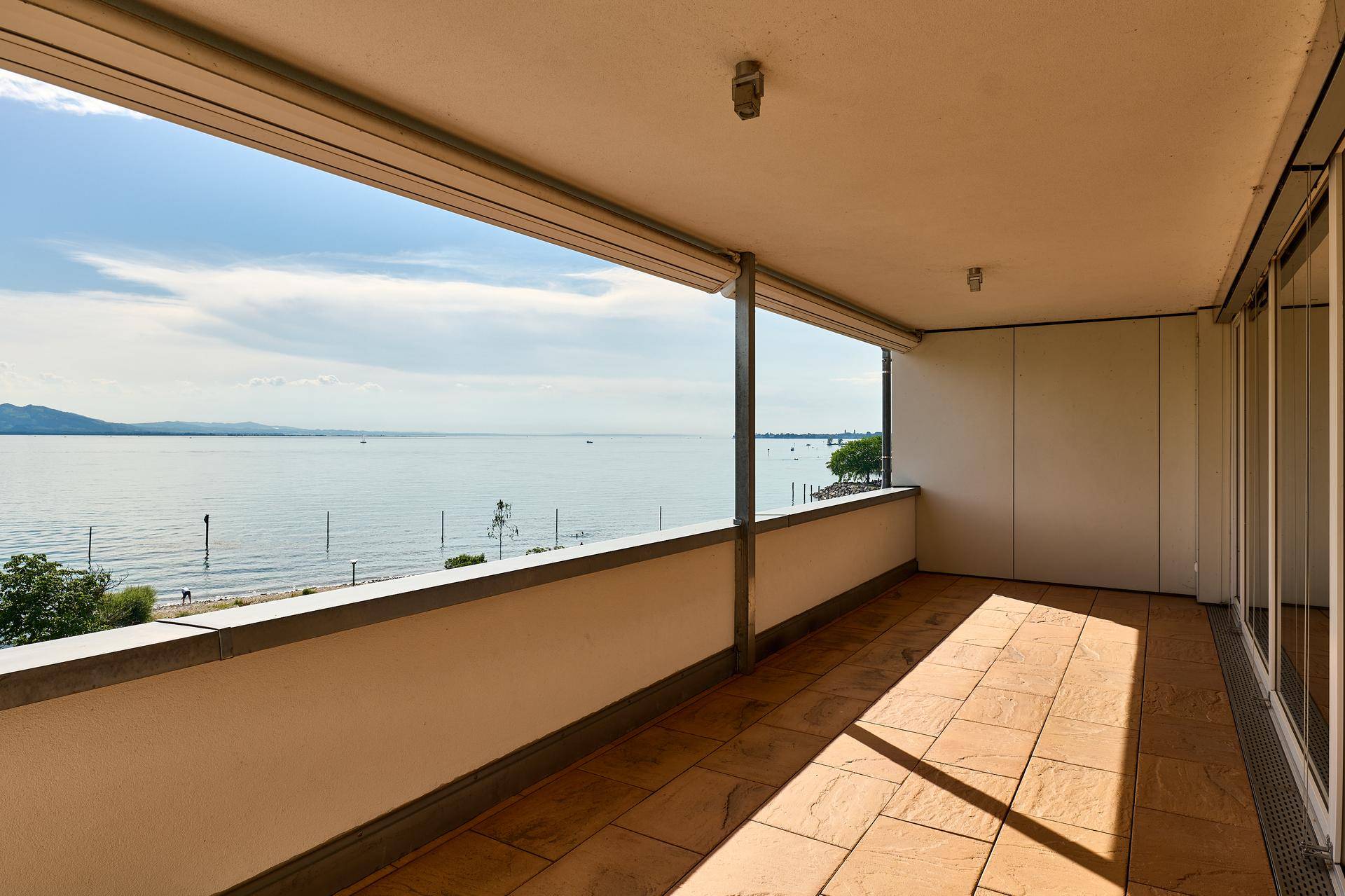 Überdachter Balkon mit Fliesenboden und einem atemberaubenden Panoramablick über den See und die umliegenden Berge.