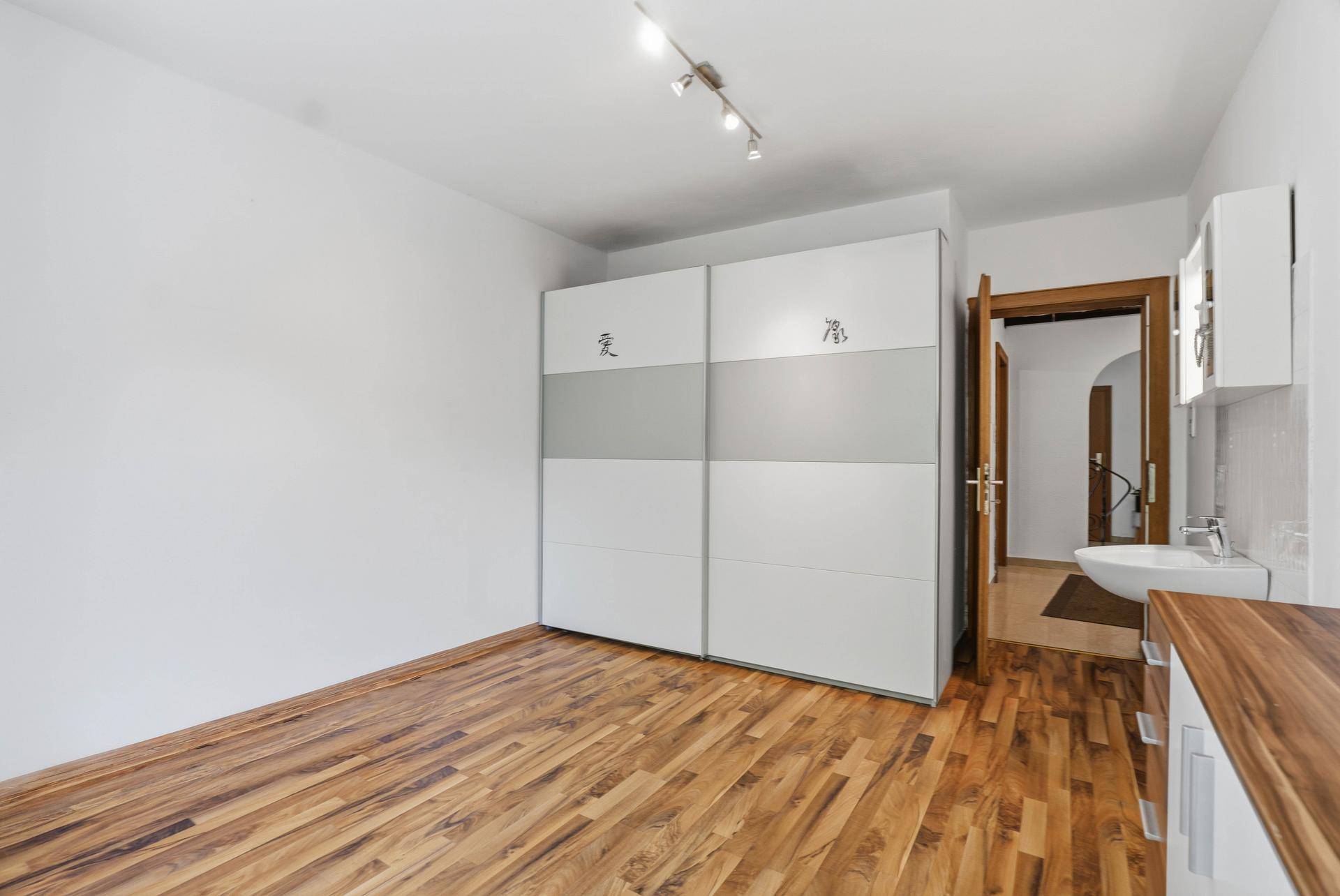 Schlafzimmer mit Holzboden, Schiebetürenschrank und integriertem Waschbecken.