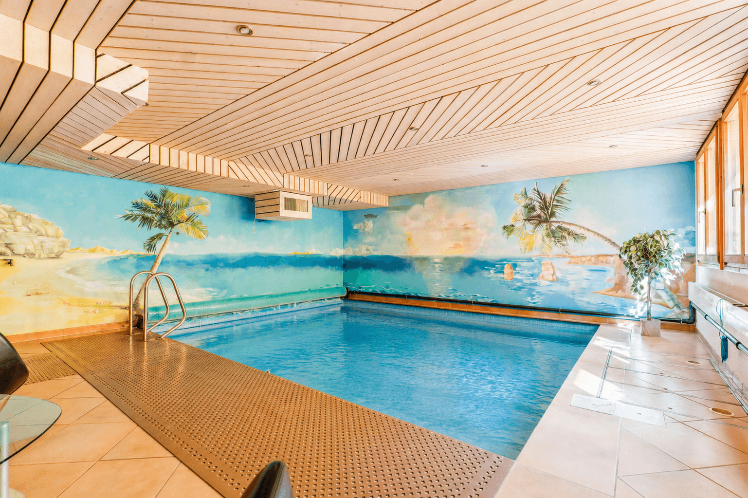 Innenpool mit Wandmalerei einer tropischen Landschaft und Holzdeckenverkleidung.