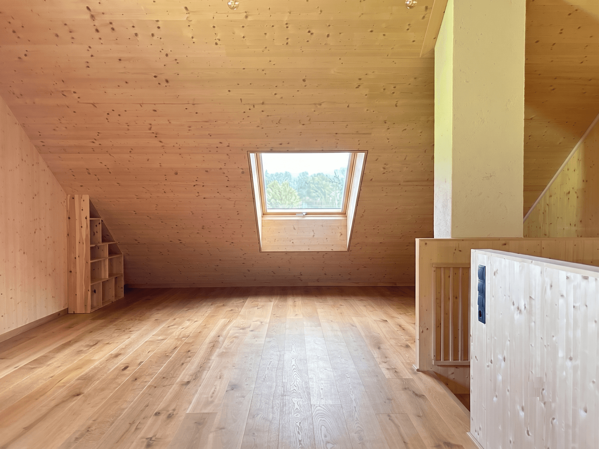 Offener Dachbodenbereich mit Holzboden, Dachfenster und integrierten Holzregalen.