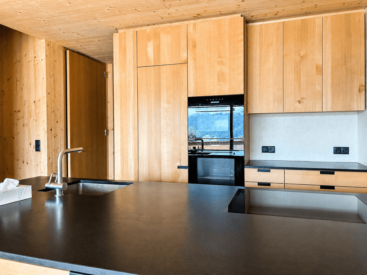 Moderne Holzküche mit dunkler Arbeitsplatte, integrierten Geräten und Bergblick.