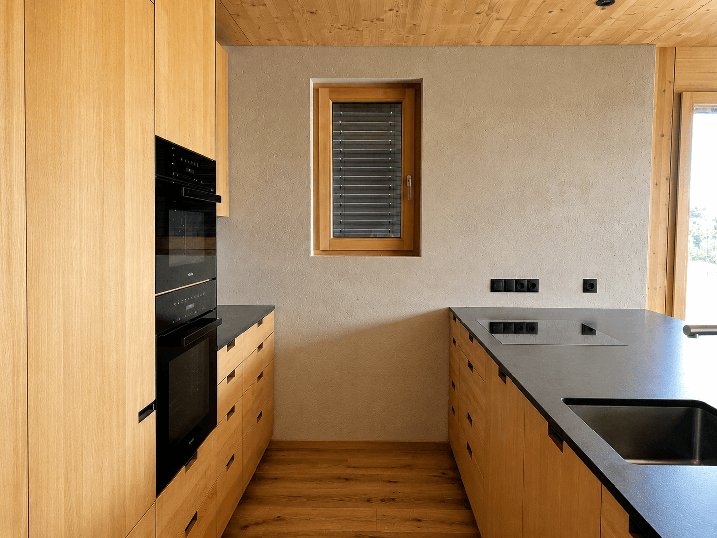 Helle Holzküche mit integrierten Geräten, dunkler Arbeitsplatte und Fenster.