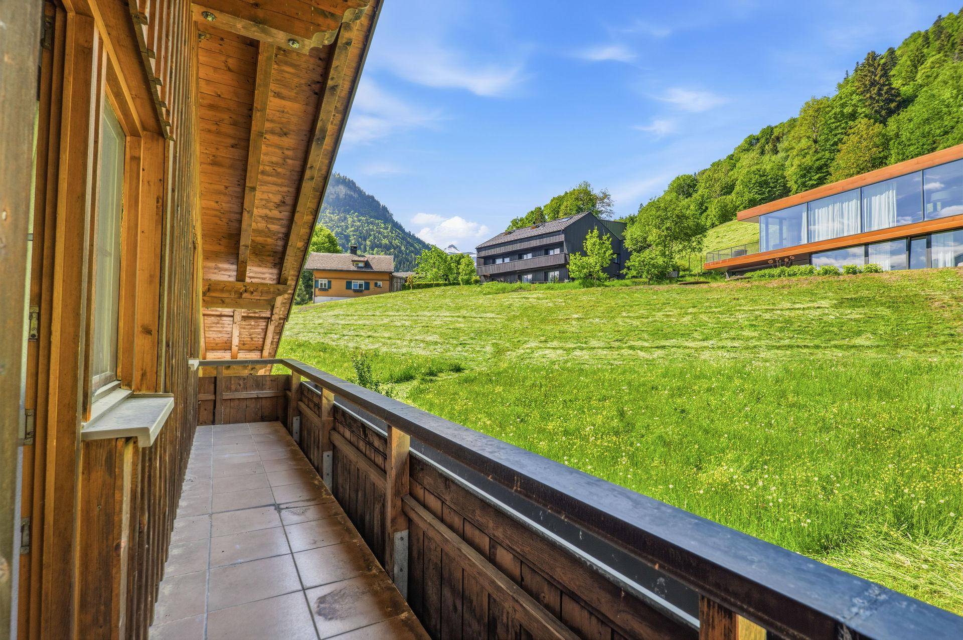 Holzbalkon mit Blick auf grüne Wiesen und die umliegende Berglandschaft.