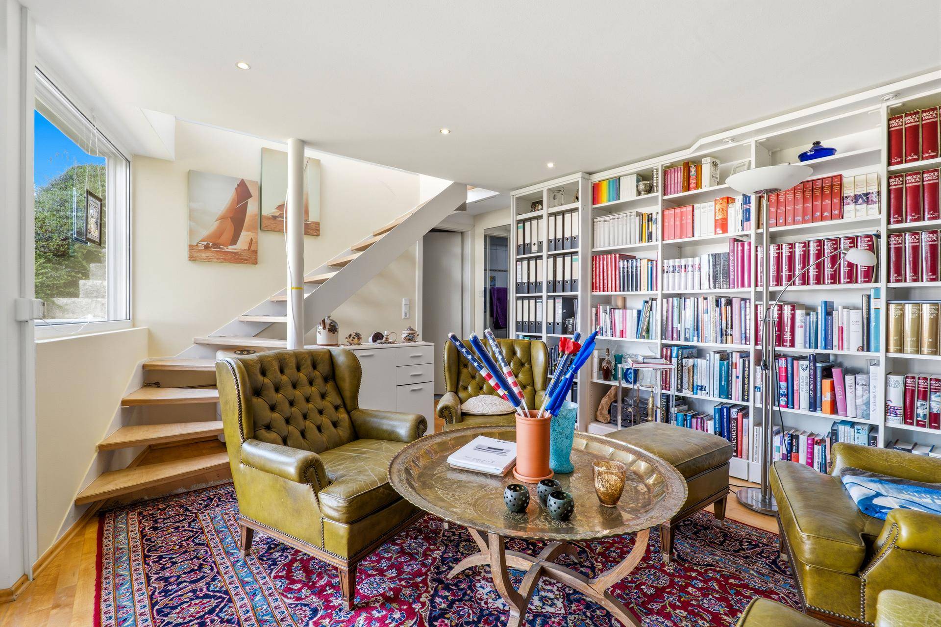 Gemütliche Bibliothek mit raumhohen Bücherregalen, Ledersesseln und einer offenen Treppe.