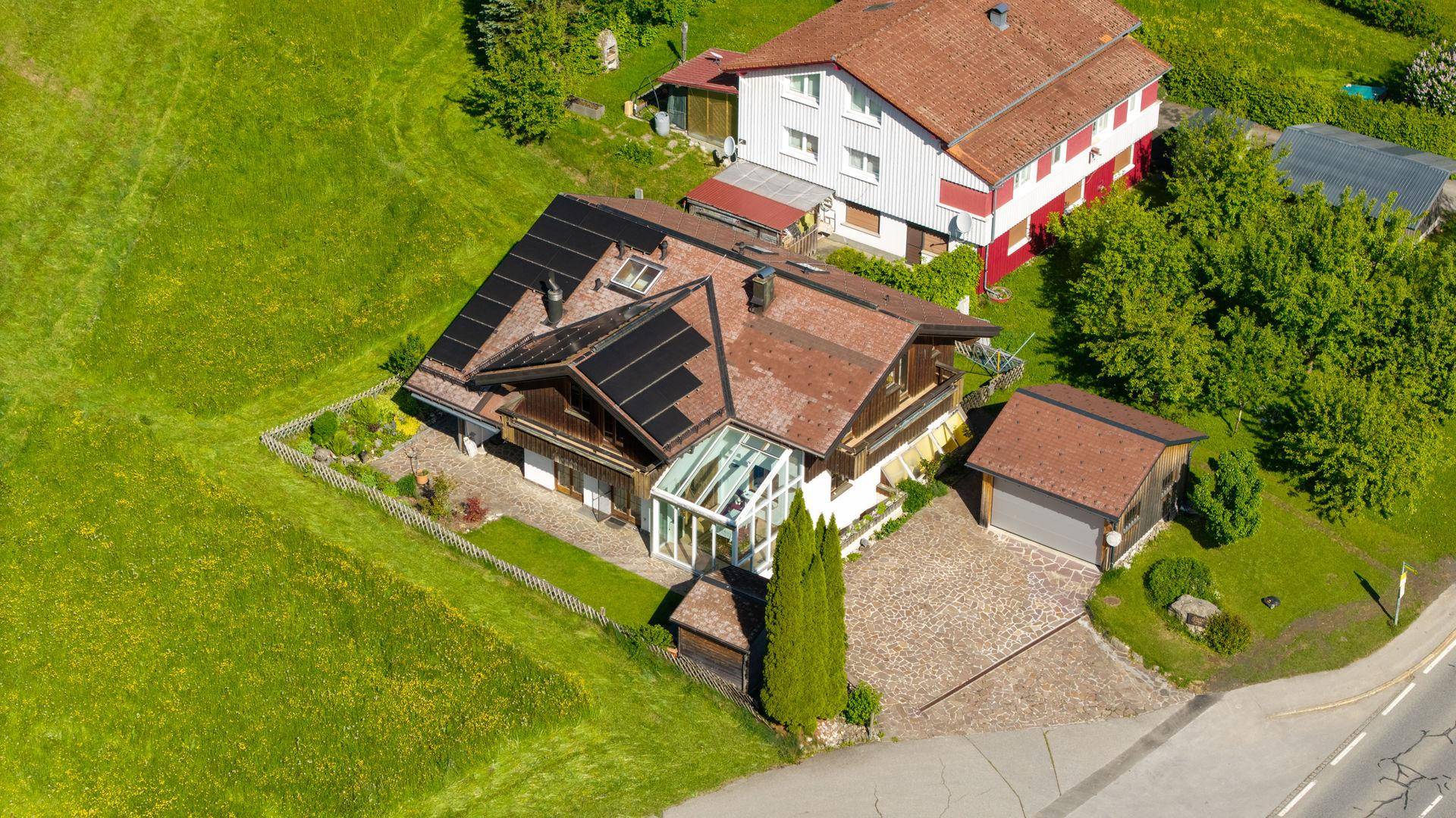 Überblick über das Anwesen mit Hauptgebäude, Wintergarten, Nebengebäude und umgebender grüner Landschaft.