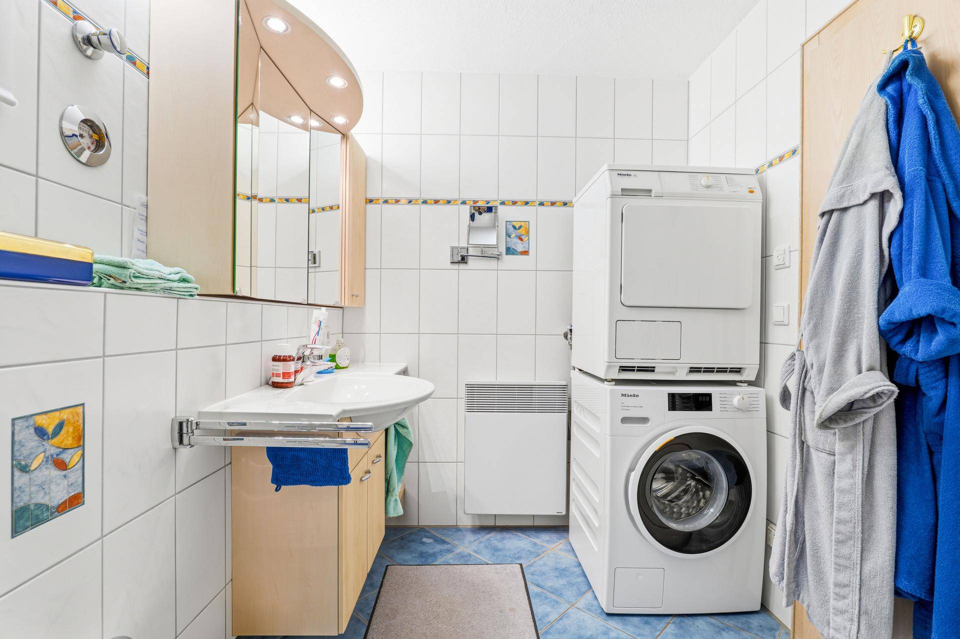 Badezimmer mit blauen Bodenfliesen, weißer Wandverkleidung und Waschmaschine sowie Trockner.