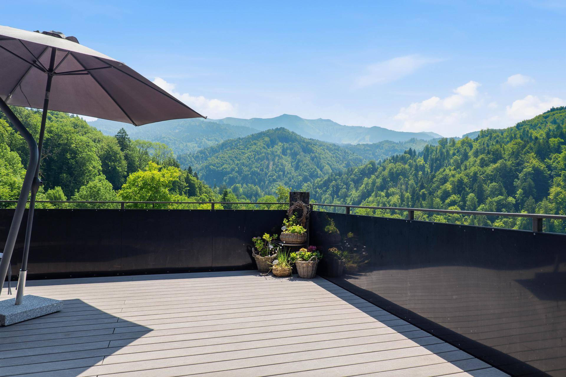 Sonnenterrasse mit weitem Bergblick, Sonnenschirm und Pflanzen.