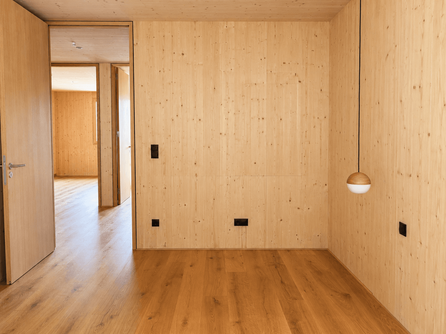 Helles Zimmer mit Holzwänden und Holzboden, bereit zur individuellen Gestaltung.
